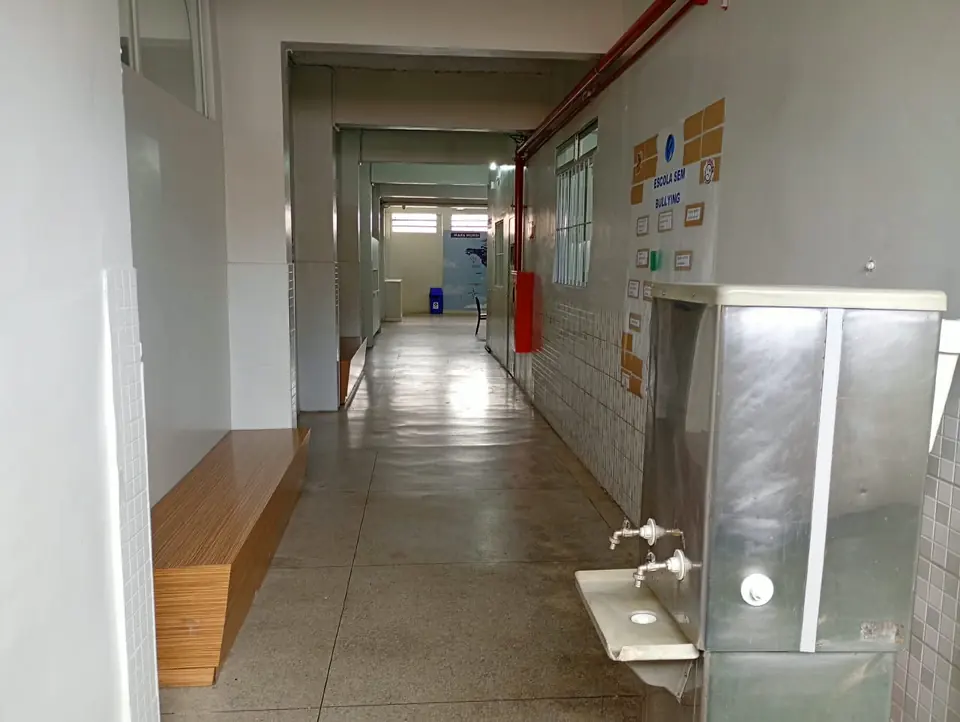 Corredor interno da escola com banco de madeira e bebedouro