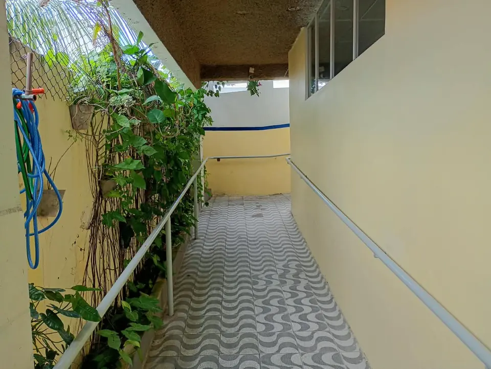 Passagem externa da escola com plantas e piso de pedra portuguesa